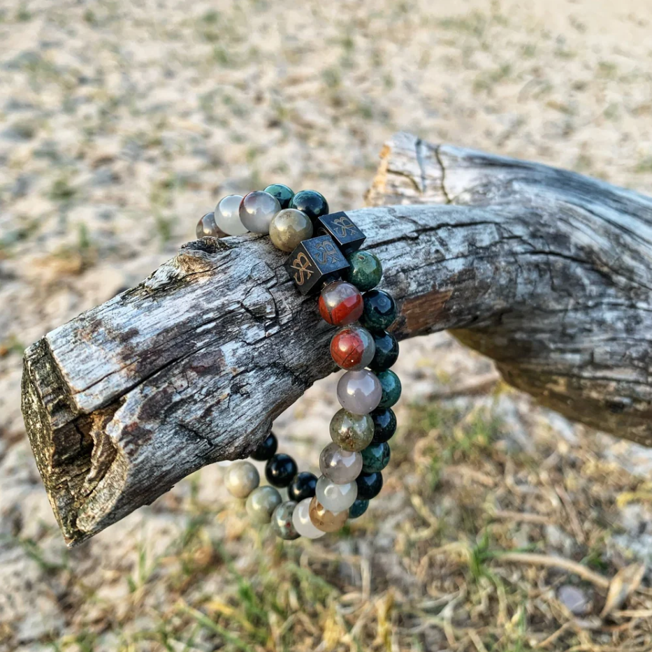Twee Stoney Bracelets armbanden, een met African Bloodstones en een met Green Tiger Eye, op verweerde tak, gefotografeerd in natuurlijke setting.