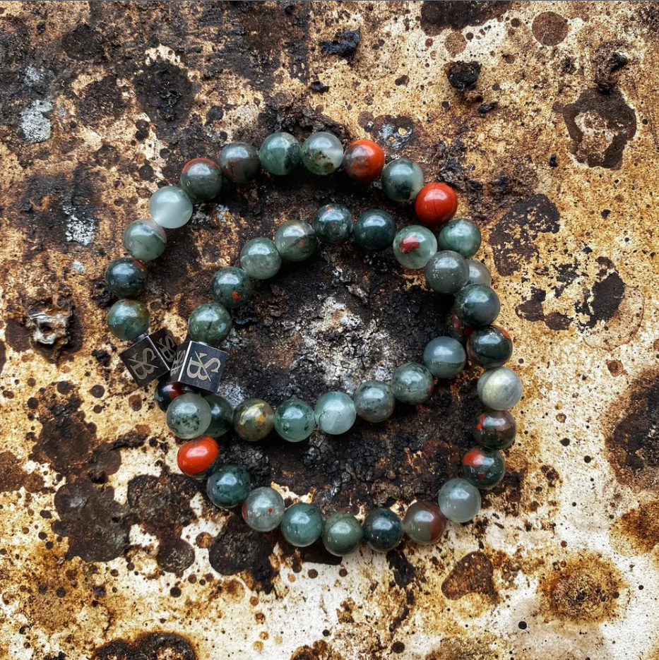 Twee African Bloodstone armbanden van Stoney Bracelets op verweerde metalen ondergrond, stoer en stijlvol.