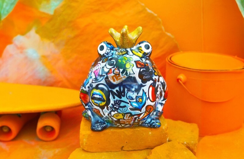 Kikker spaarpot met gouden kroontje en kleurrijk graffiti-design van het merk Pomme-Pidou, verkrijgbaar bij cadeauwinkel Omdat in Uden.